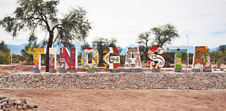 letras verticales pintadas con guardas coloridas en una plaza formando la palabra Tinogasta