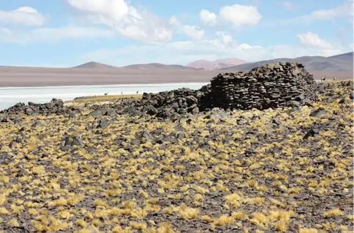 pared pircada delas ruinas del tambo en un paisaje yermo al fondo la laguna y las cumbres de los Andes Nevados