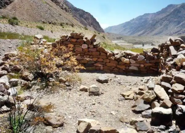 pared de piedra bocha de las ruinas, al fondo la cordillera y puente ferroviario
