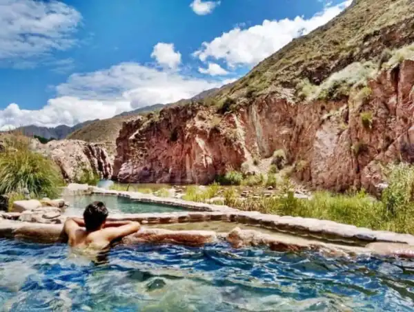 hombre en pileta termal al aire libre entre barrancos de rocas